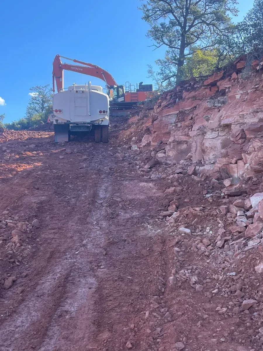 White dump truck and excavator on a steep red dirt hillside under a blue sky
