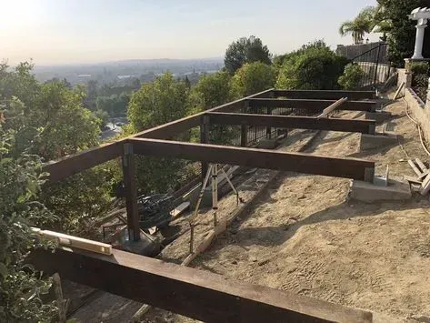 Wooden deck under construction on a hillside with a valley view and trees at sunset