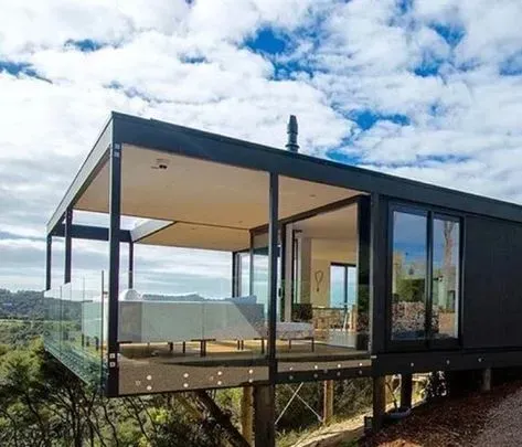 Modern black house with large glass windows and a covered deck overlooking a green landscape.