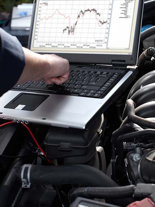 A man is working on a car engine with a laptop
