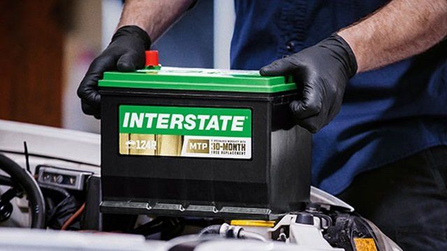 A man is holding a battery in front of a car.