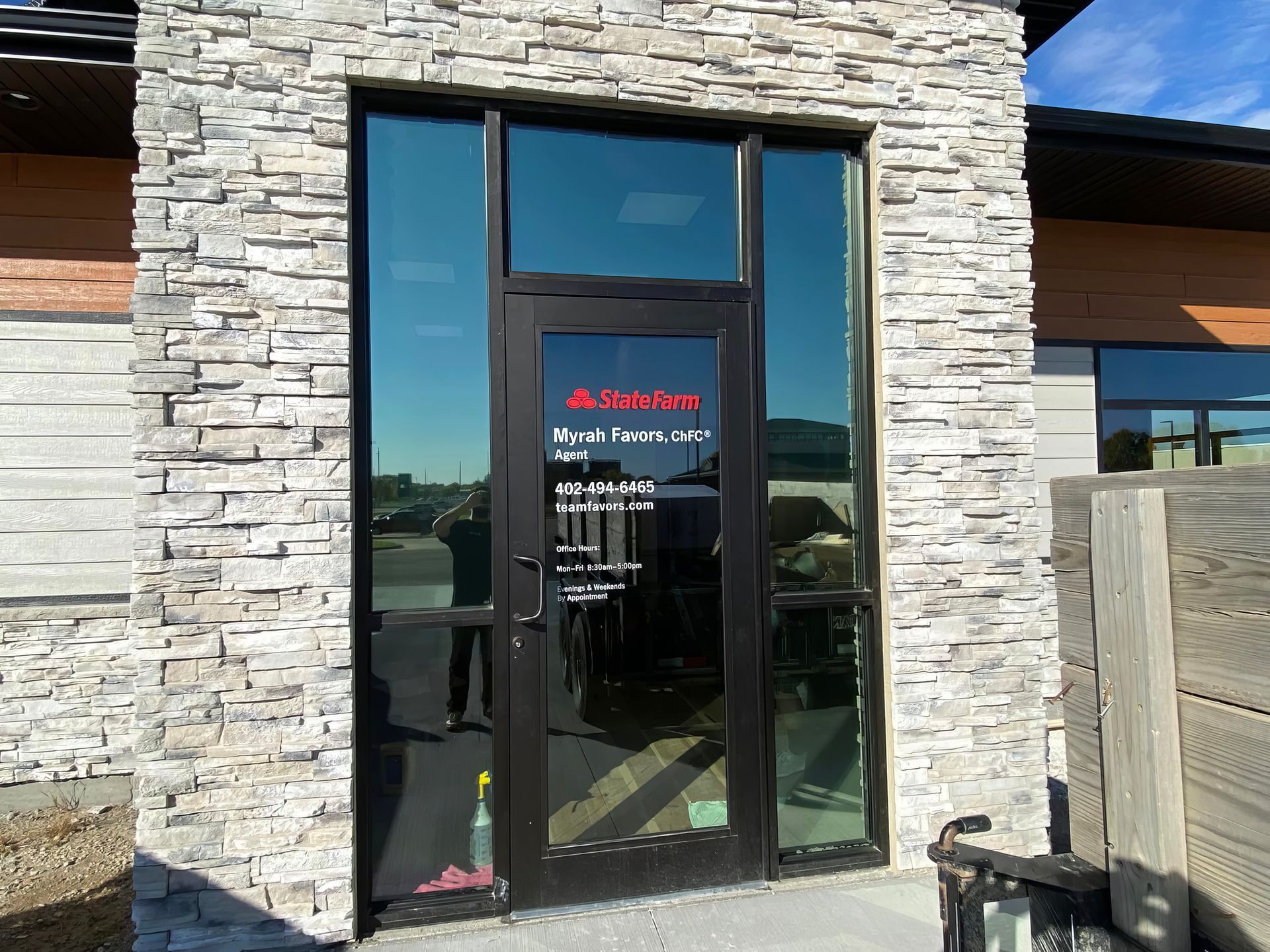 Glass storefront entrance in stone wall with black double doors and red signage