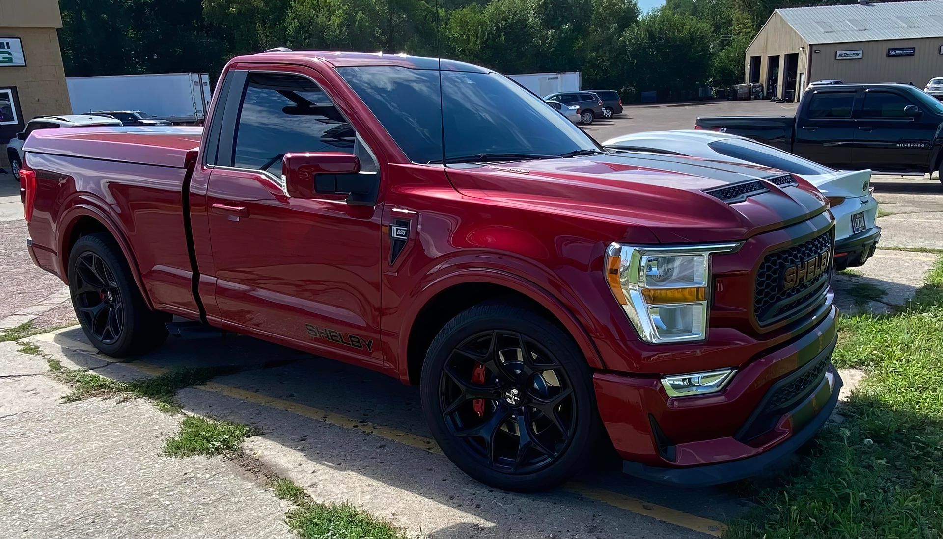 Red pickup truck parked on a driveway in front of a house, with another vehicle in the background.