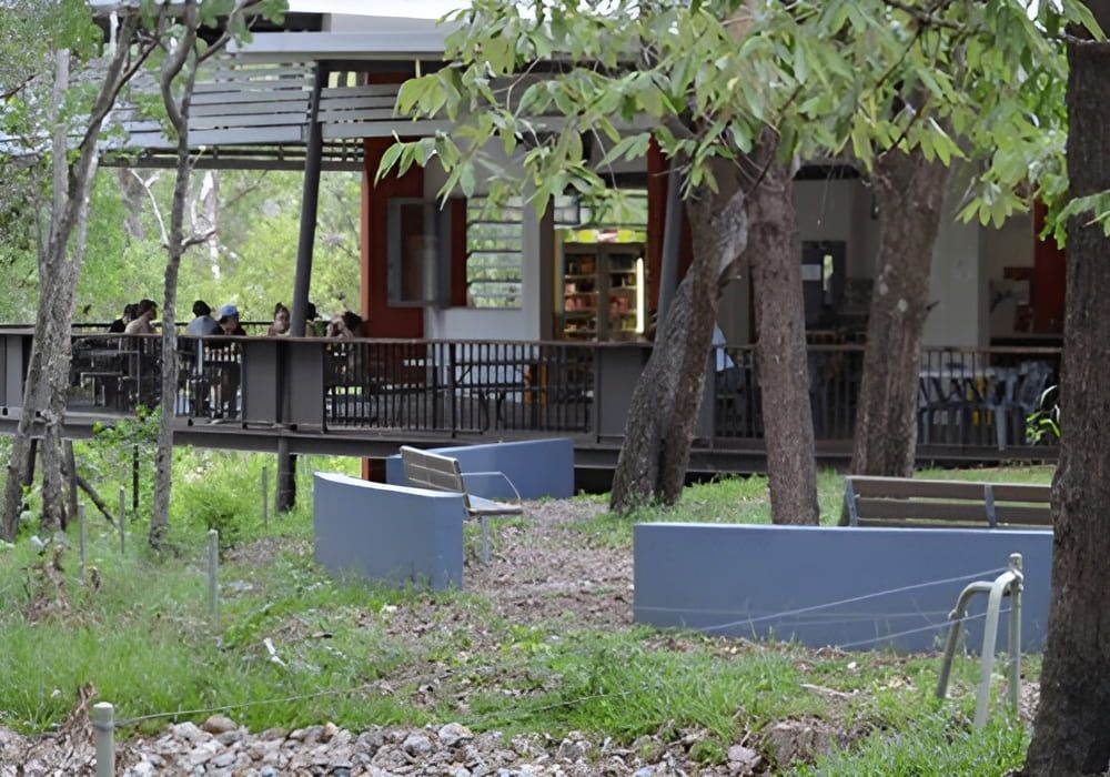 A Group Of People Are Sitting Outside Of A Building Surrounded By Trees — Jakes Steel & Welding in East Arm, NT