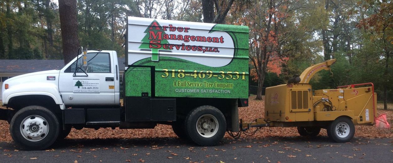 White utility truck towing a yellow wood chipper on a leaf-covered road in autumn