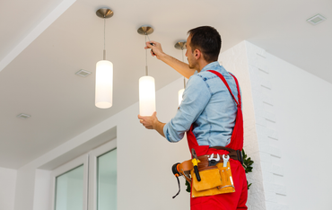 Electrician in red overalls installing ceiling pendant lights in a bright room
