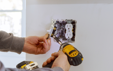 Hands wiring a wall outlet during new electrical installation
