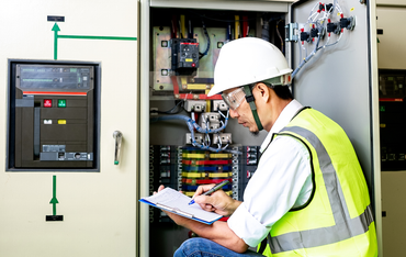 Technician in hard hat inspecting an open electrical panel