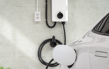 White electric car charging at a wall-mounted EV charger in a garage