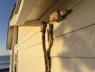 Rusty metal object mounted on the side of a white building near the ocean