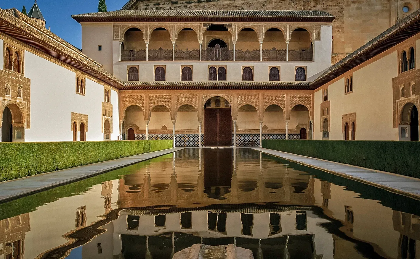 Courtyard of the Alhambra reflecting pool, with arched walkways, detailed carvings, and beige walls, in Granada, Spain.