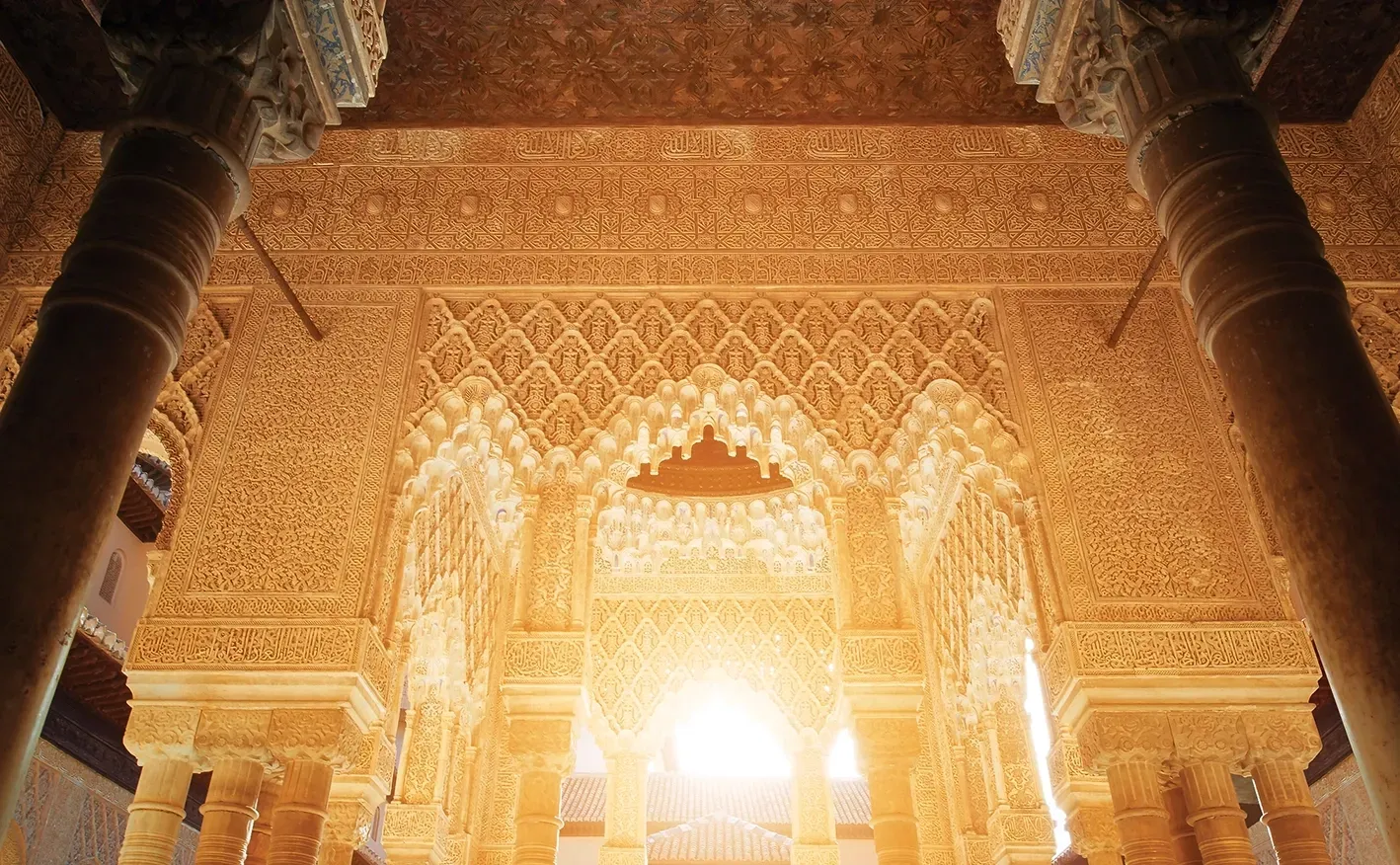 Intricate arched doorways and columns with detailed carvings inside a building lit by bright sunlight.