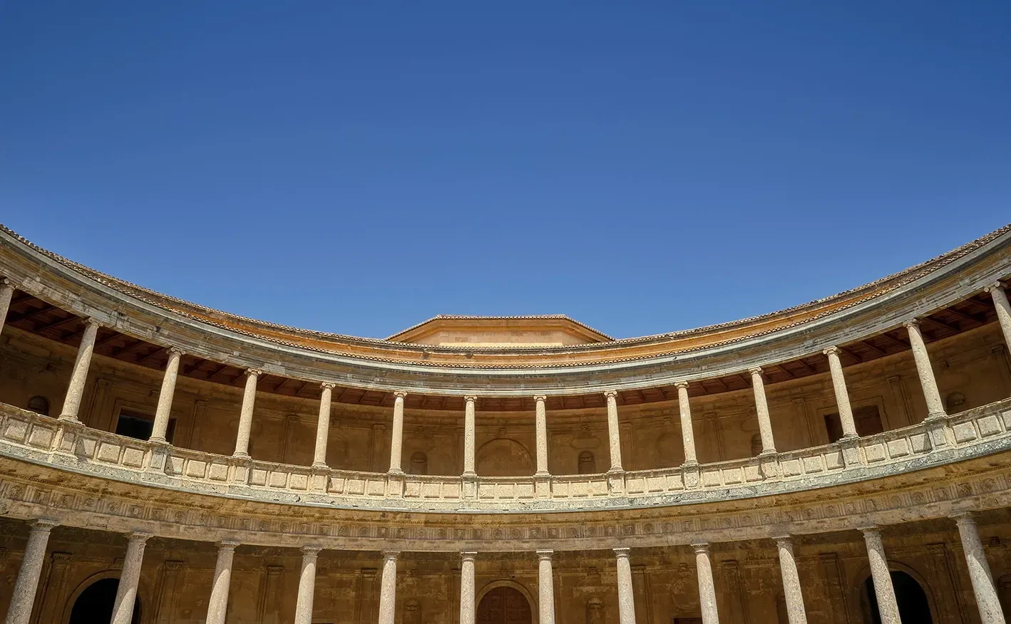 A low-angle view of the circular, two-story stone courtyard of the Palace of Charles V, featuring rows of columns.