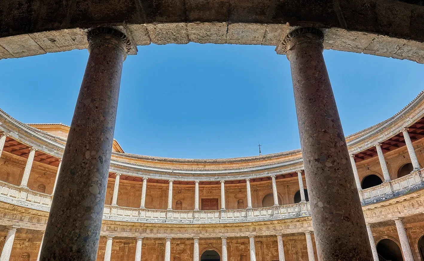 Courtyard of the Charles V Palace, Granada, Spain, viewed from below through columns, with blue sky above.