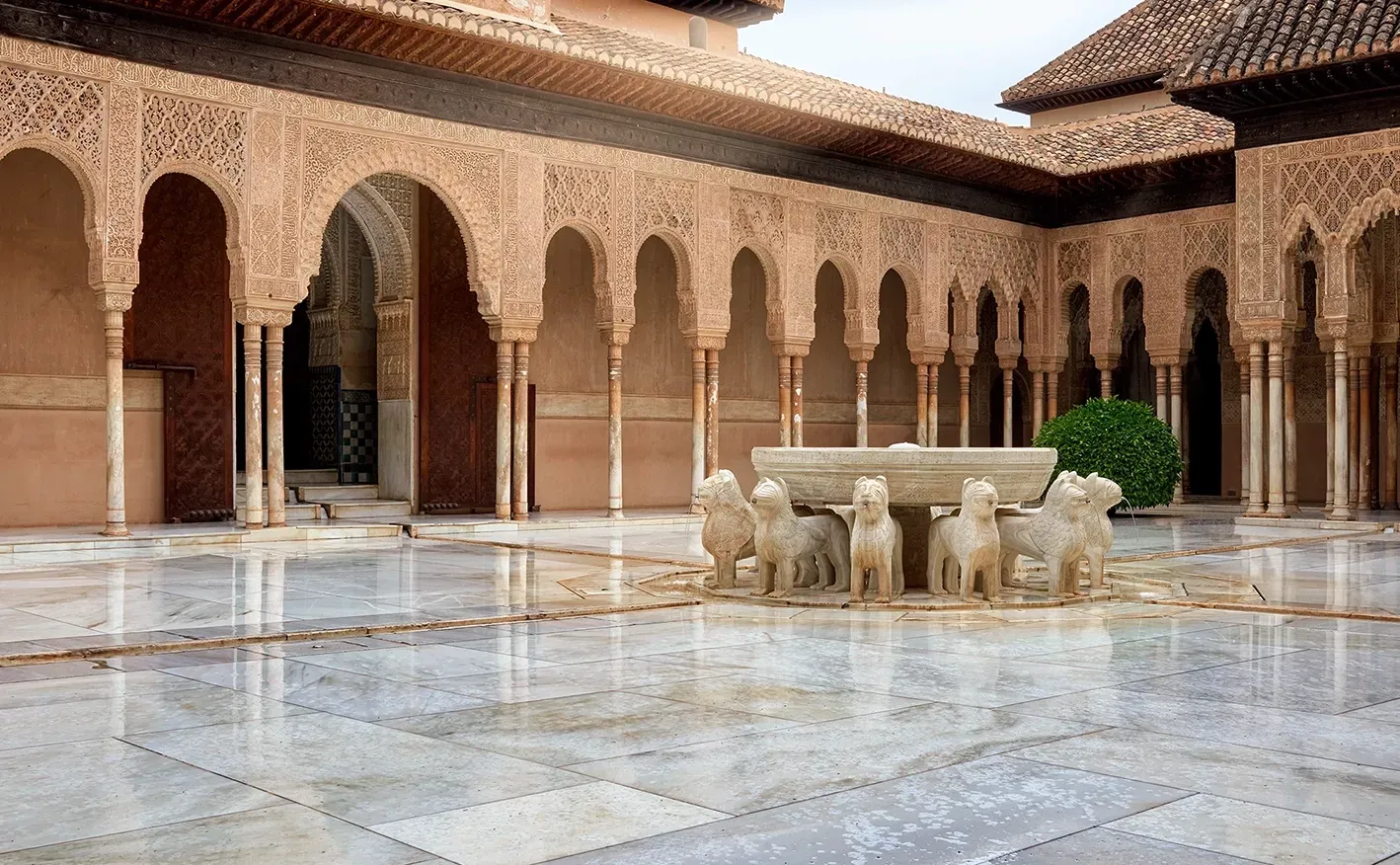 Courtyard in the Alhambra with arched colonnade, marble floor, and fountain with lion sculptures.