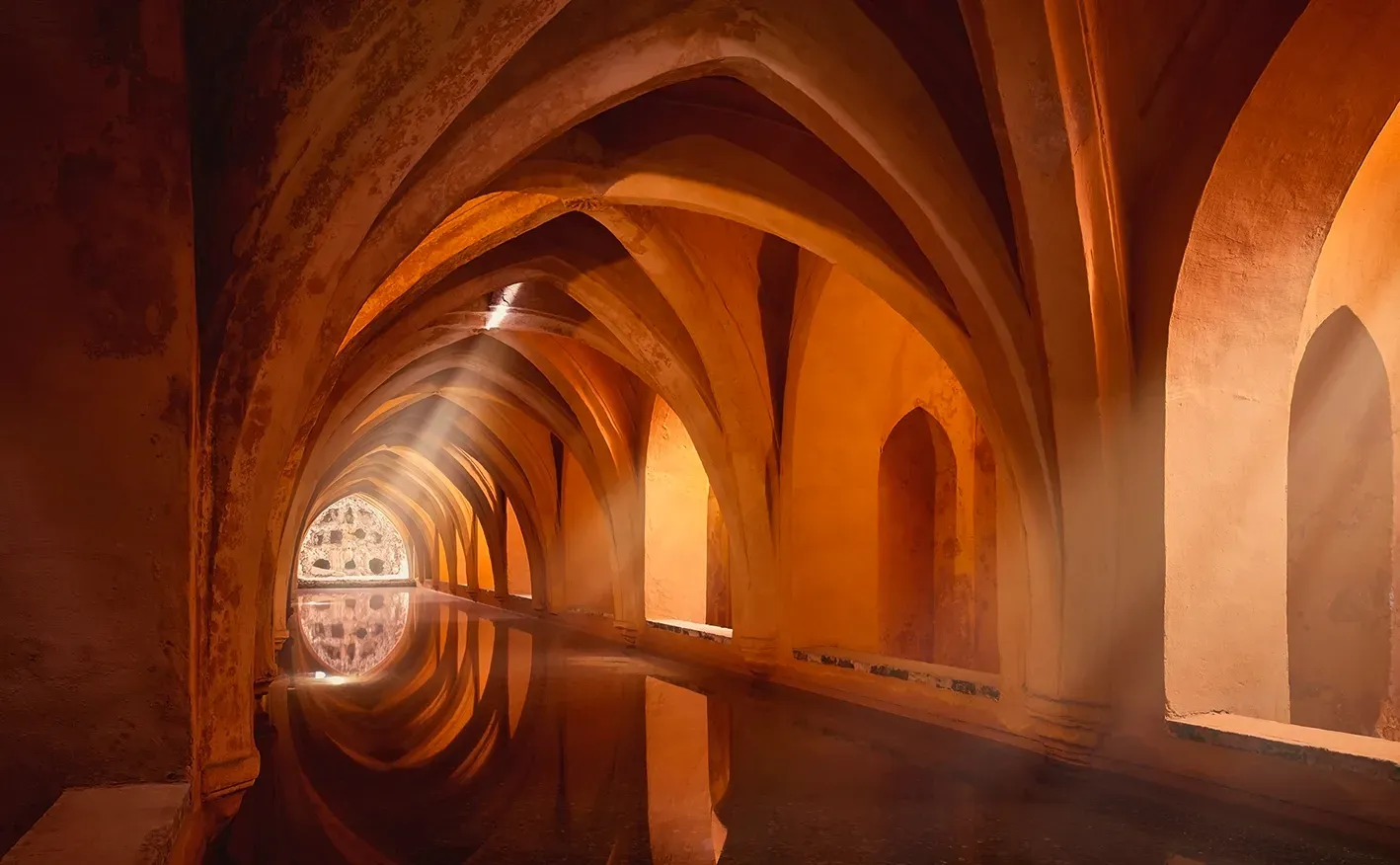 Arched, orange-toned hall with a reflecting pool. Sunlight streams in from a far window.