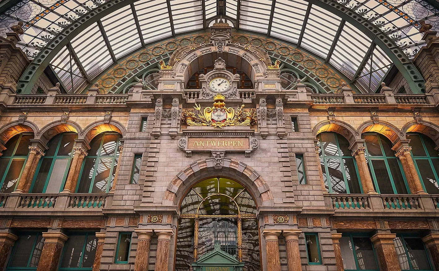 Ornate stone facade of Antwerp Central Station with clock and arched windows.