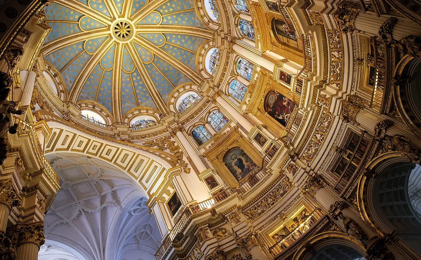 Ornate, golden interior of a cathedral dome with blue ceiling and detailed architectural elements.