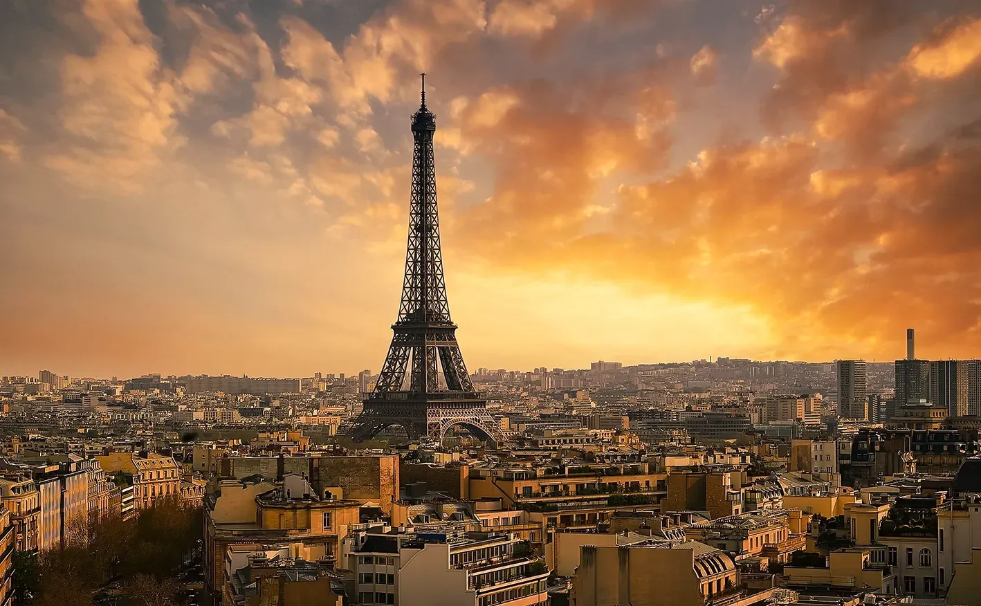 Eiffel Tower against a sunset sky over Paris rooftops.