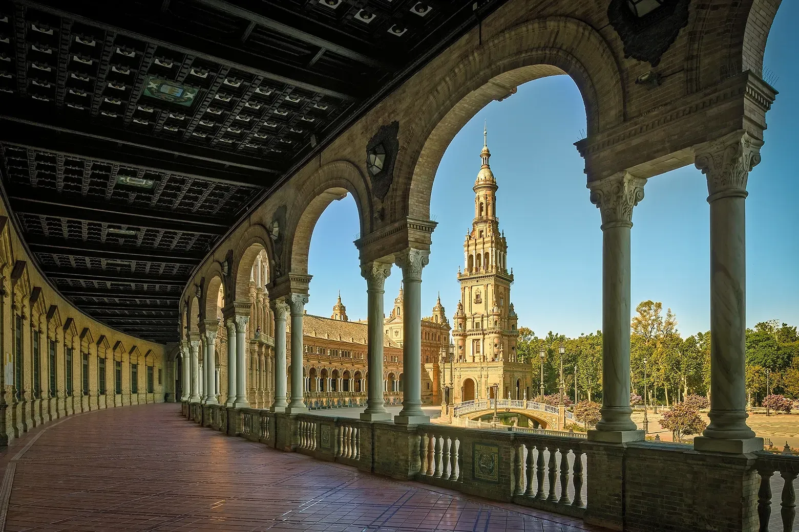 Arcaded walkway frames a view of a bell tower in Seville, Spain.