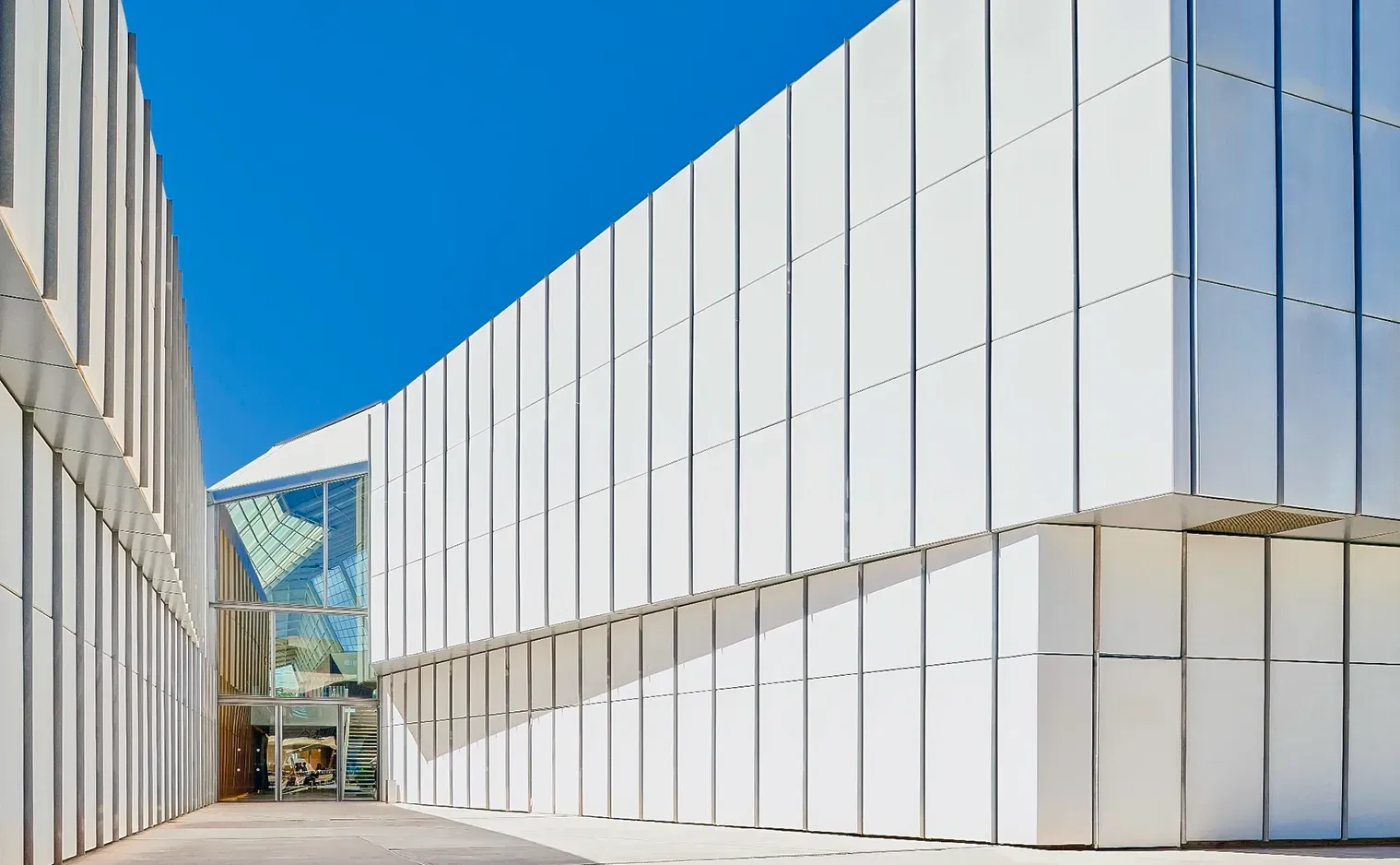 White modern building exterior with a clear glass entrance against a bright blue sky.