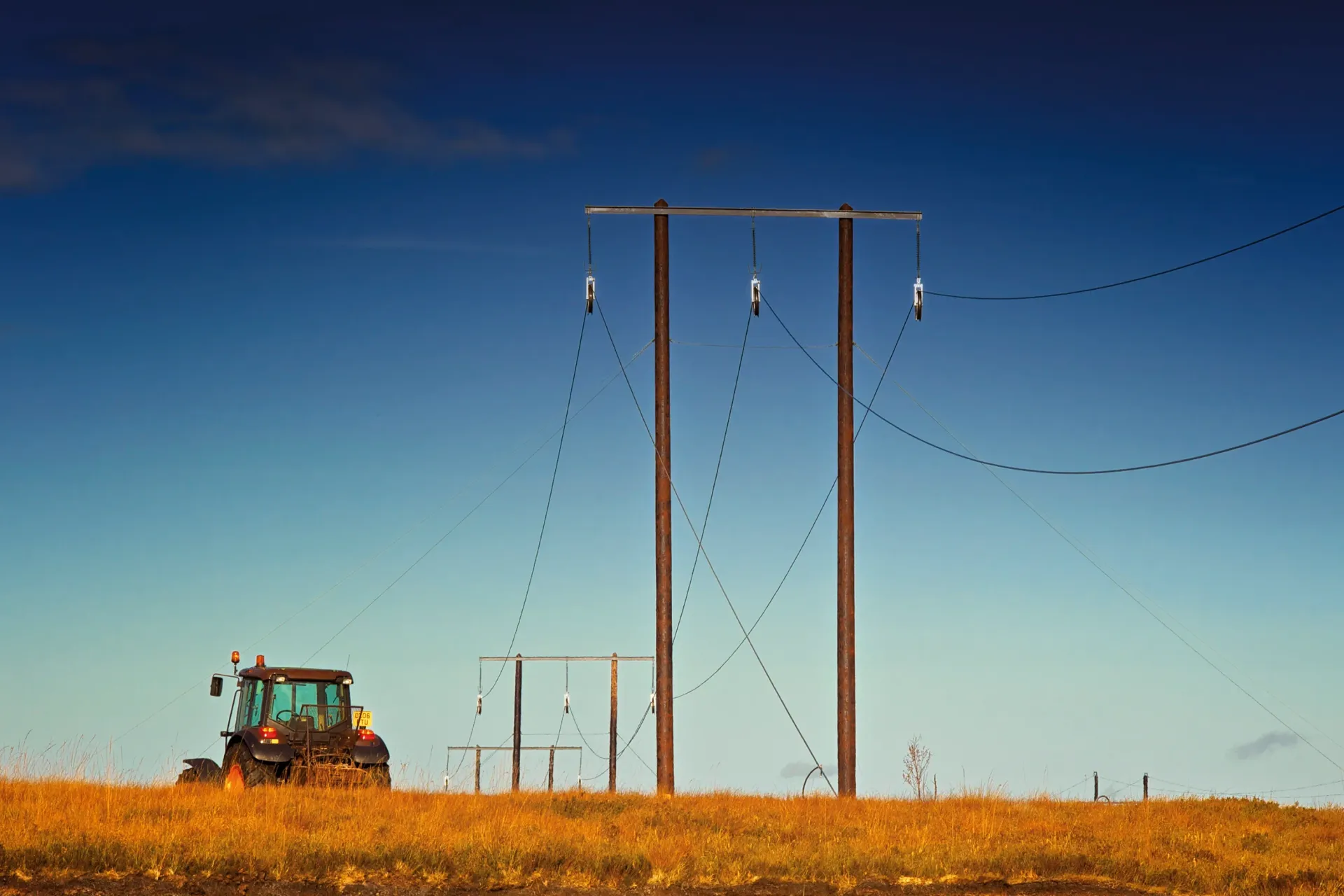 Tractor on a grassy field with power lines under a blue sky.