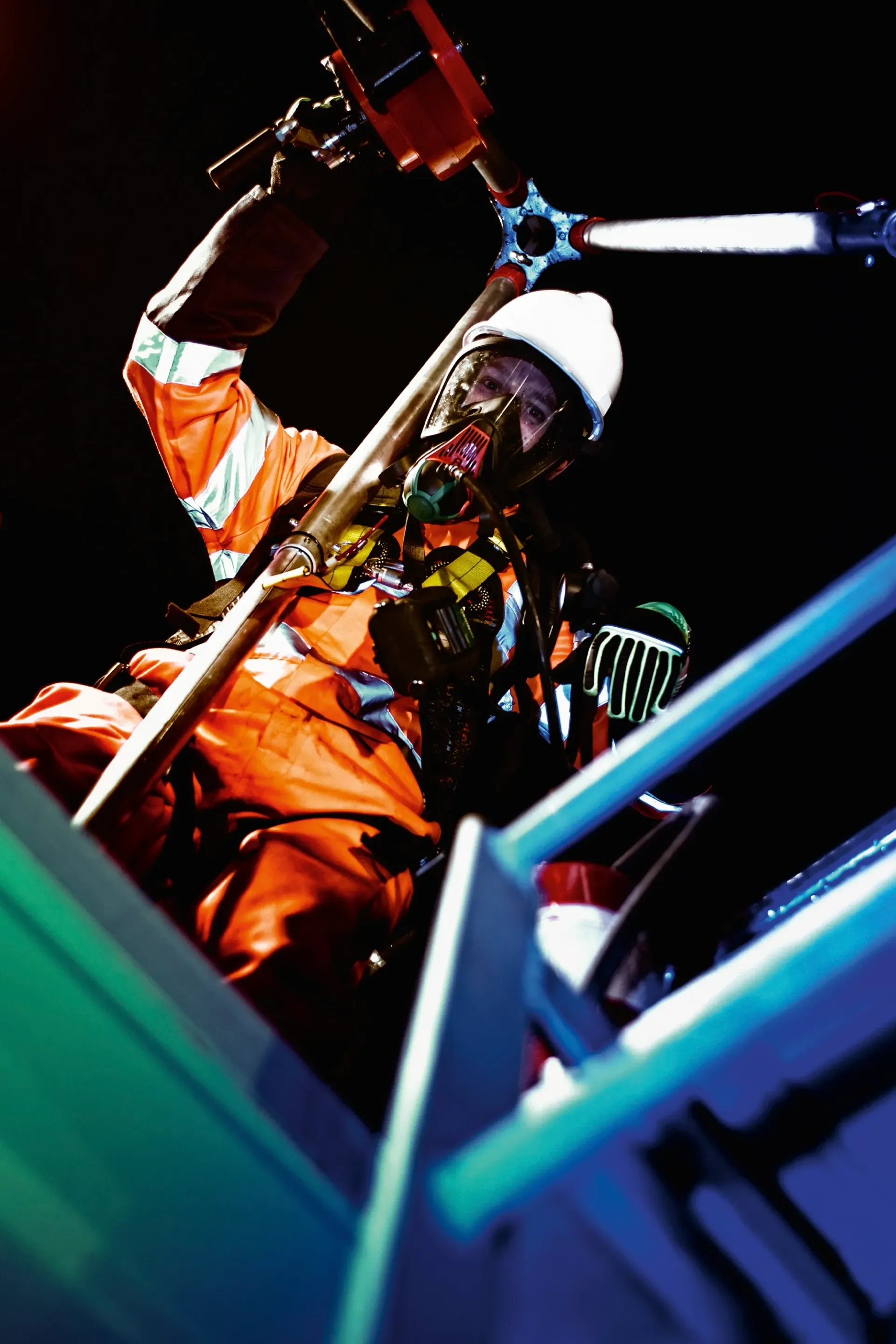 Person in orange protective gear working on machinery, wearing a respirator mask and hard hat.