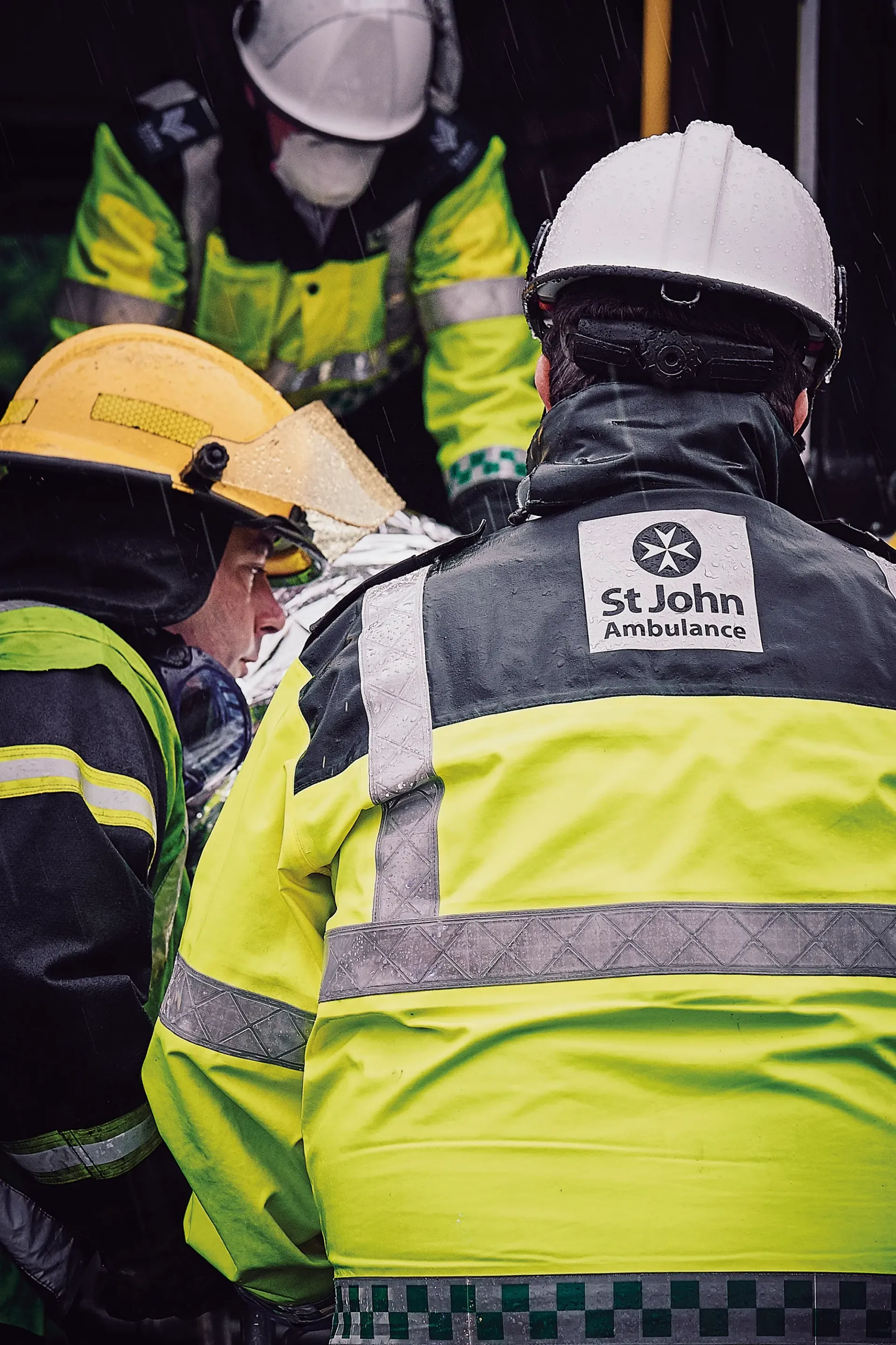 Emergency responders in yellow and white helmets assist a person on a stretcher.