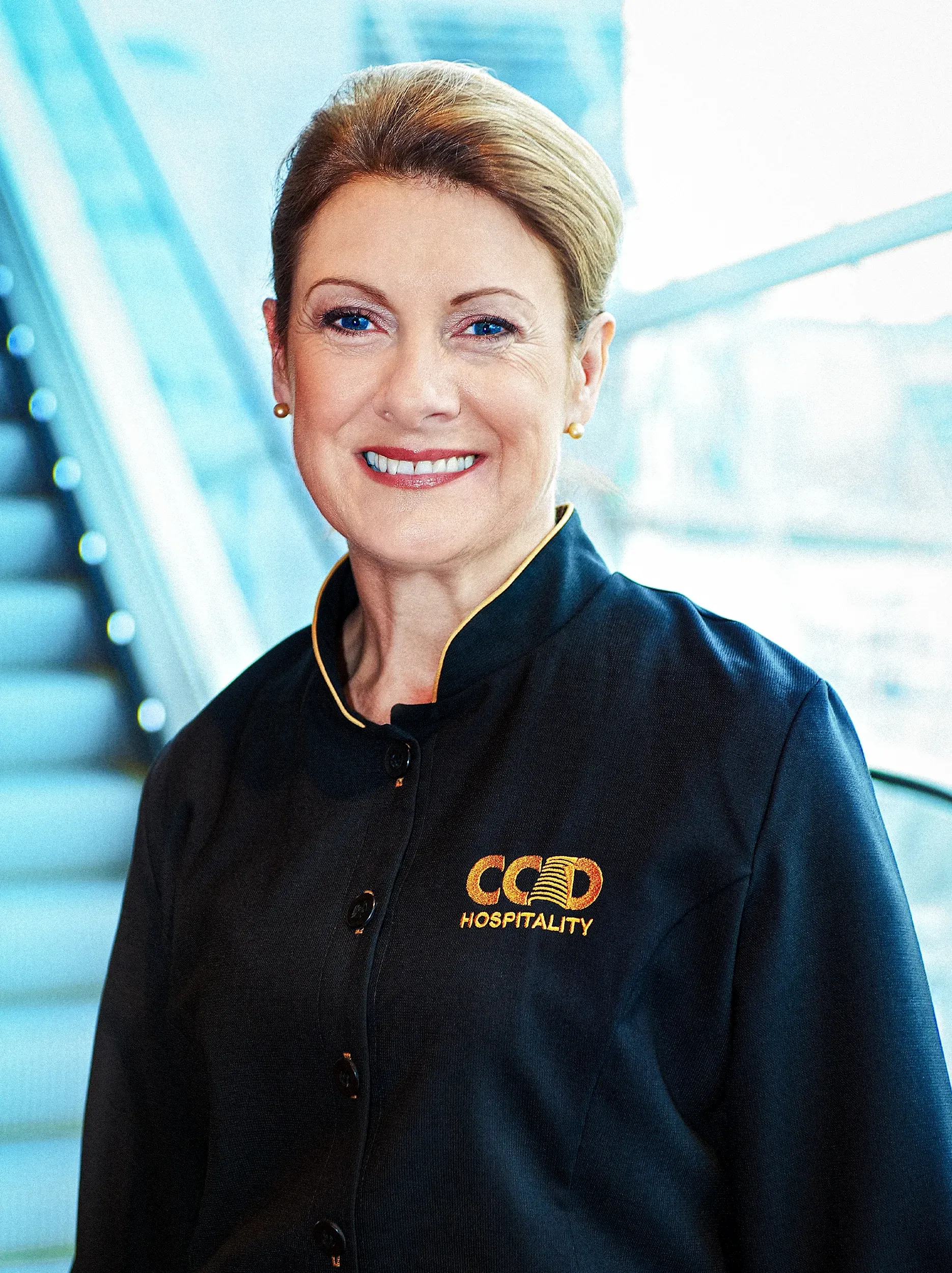 Woman in a black jacket with gold trim, smiling, with