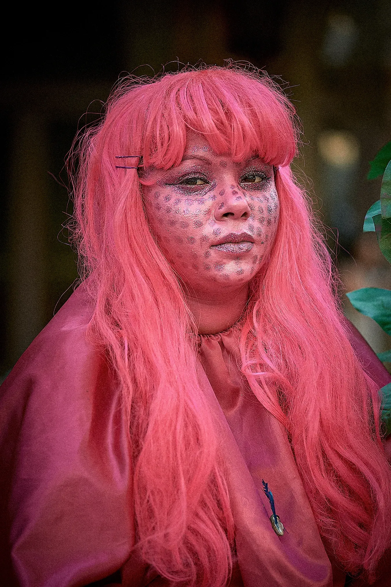 Person with pink hair, skin, and outfit, with dark spots on face.