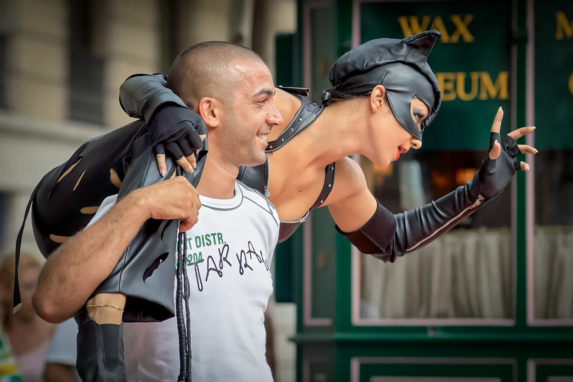 Man carrying a person dressed as Catwoman, posing near a building with