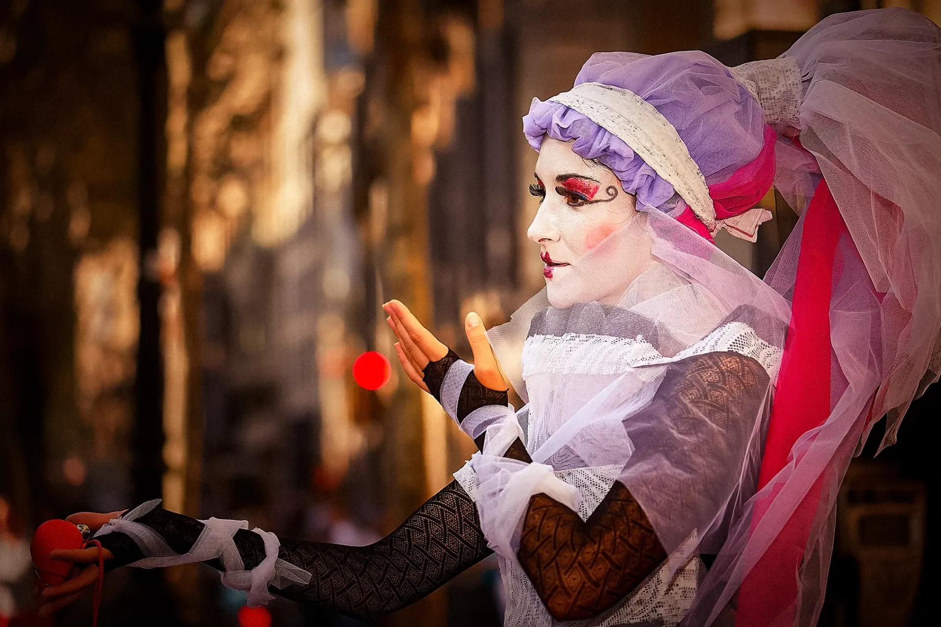 Street performer in elaborate makeup and costume gestures with hands, colorful headdress.