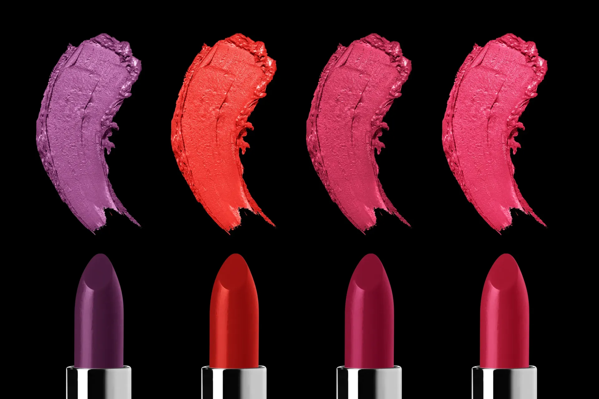 Four lipstick tubes with swatches in purple, red, and pink shades against a black background.