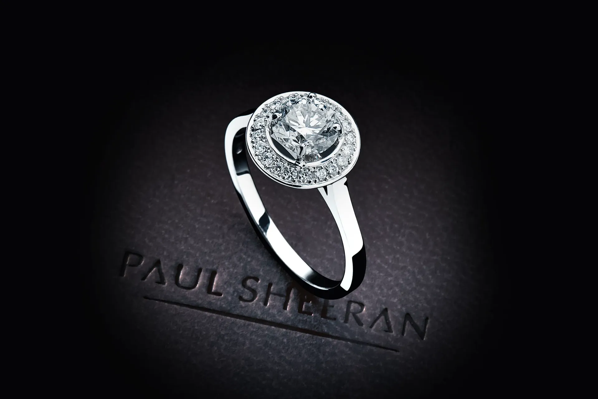 Diamond ring on a black surface; Paul Sheeran logo visible.