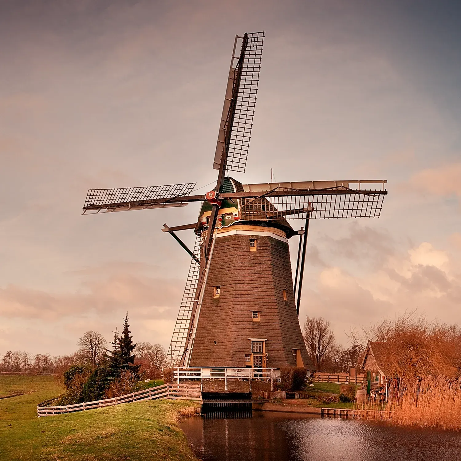 Dutch windmill by water, cloudy sky.
