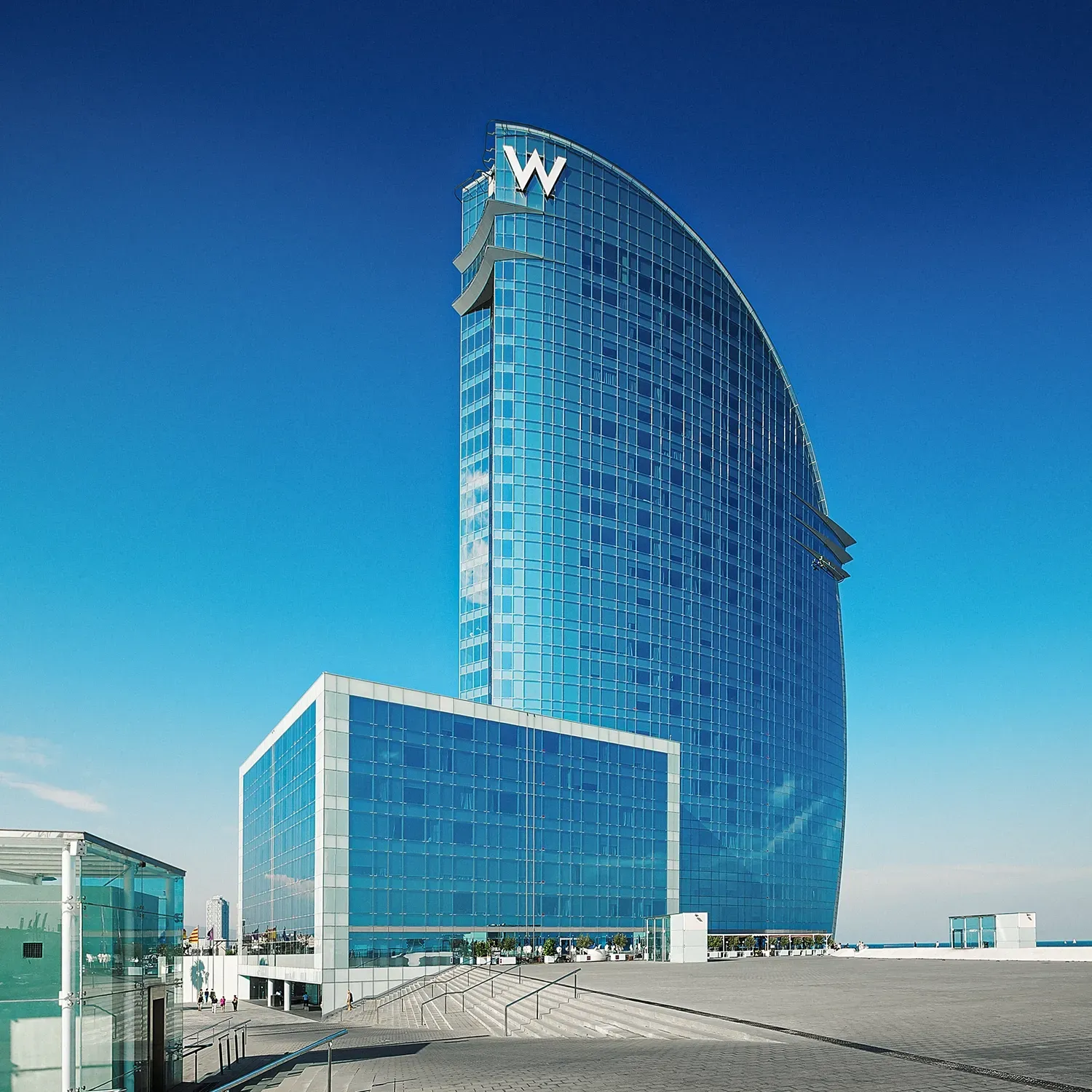 W Hotel, Barcelona, Spain, a modern, sail-shaped blue glass building under a clear blue sky.