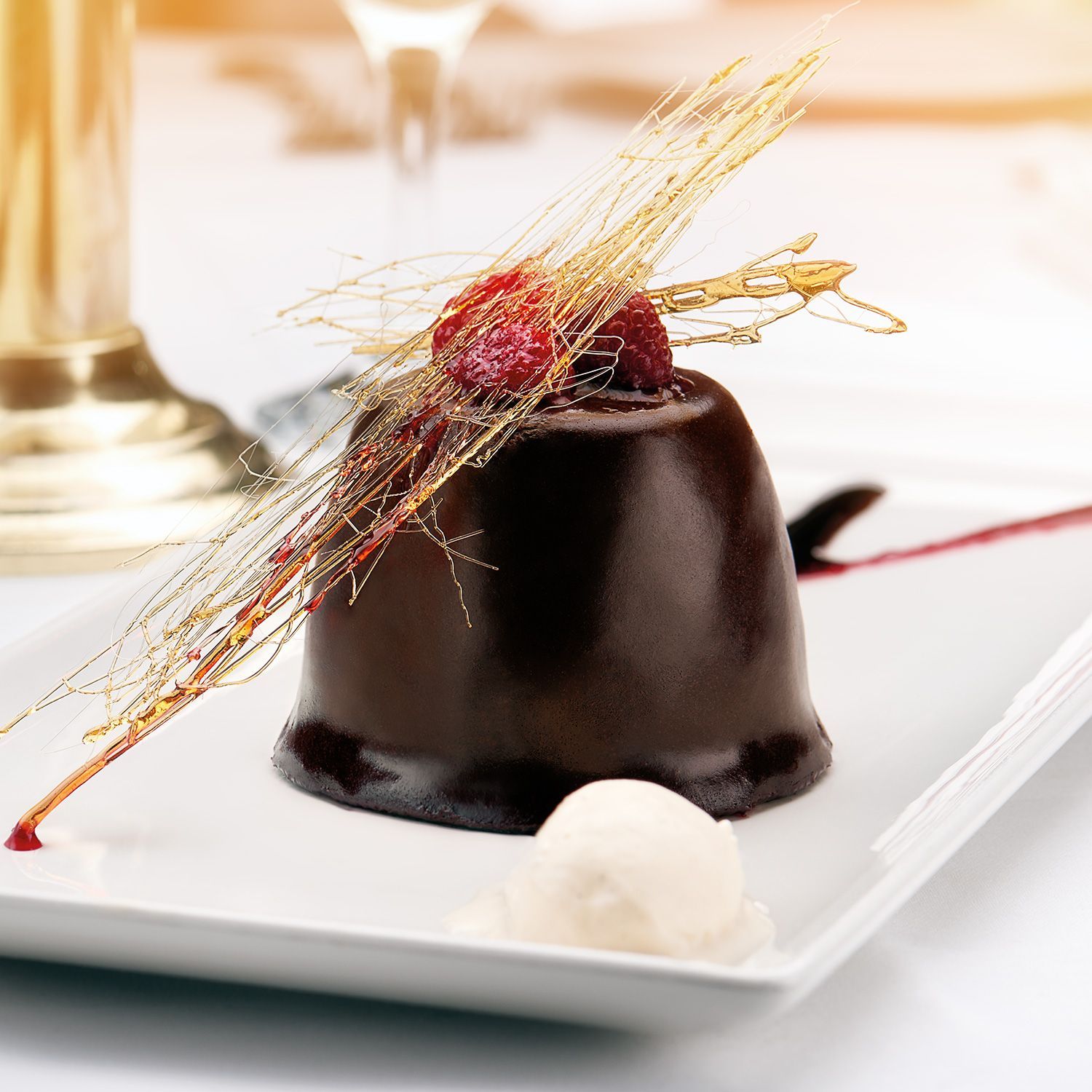 Chocolate dessert with raspberry and caramel garnish on white plate, ice cream.