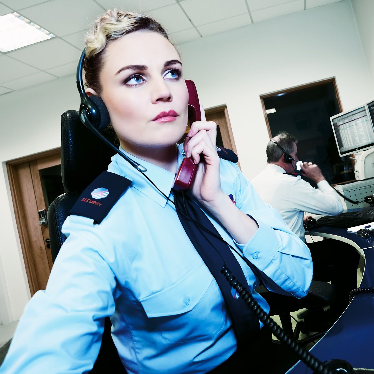 Woman in uniform, using a headset and telephone, in a dispatch center.