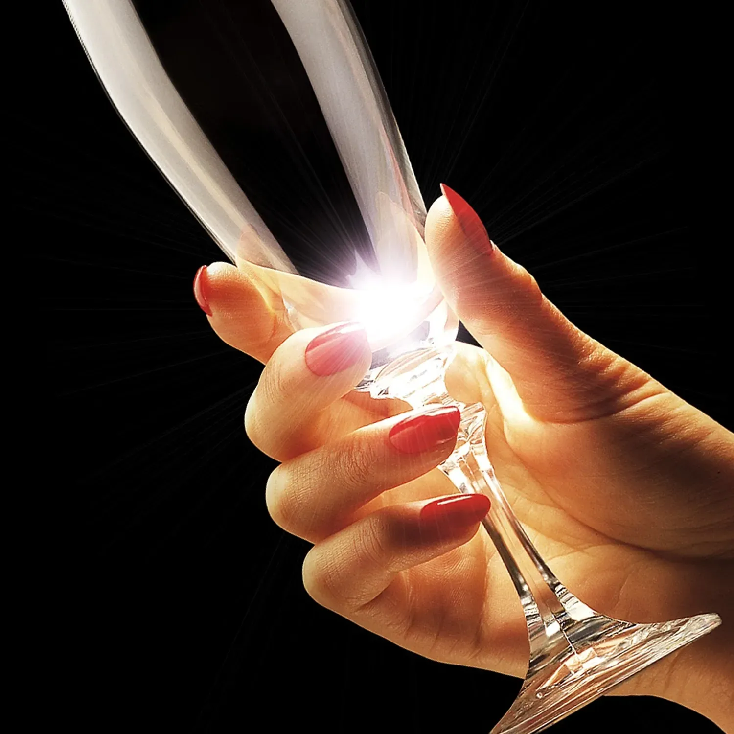 Hand holding a champagne flute against a black background, with bright light shining through the glass.