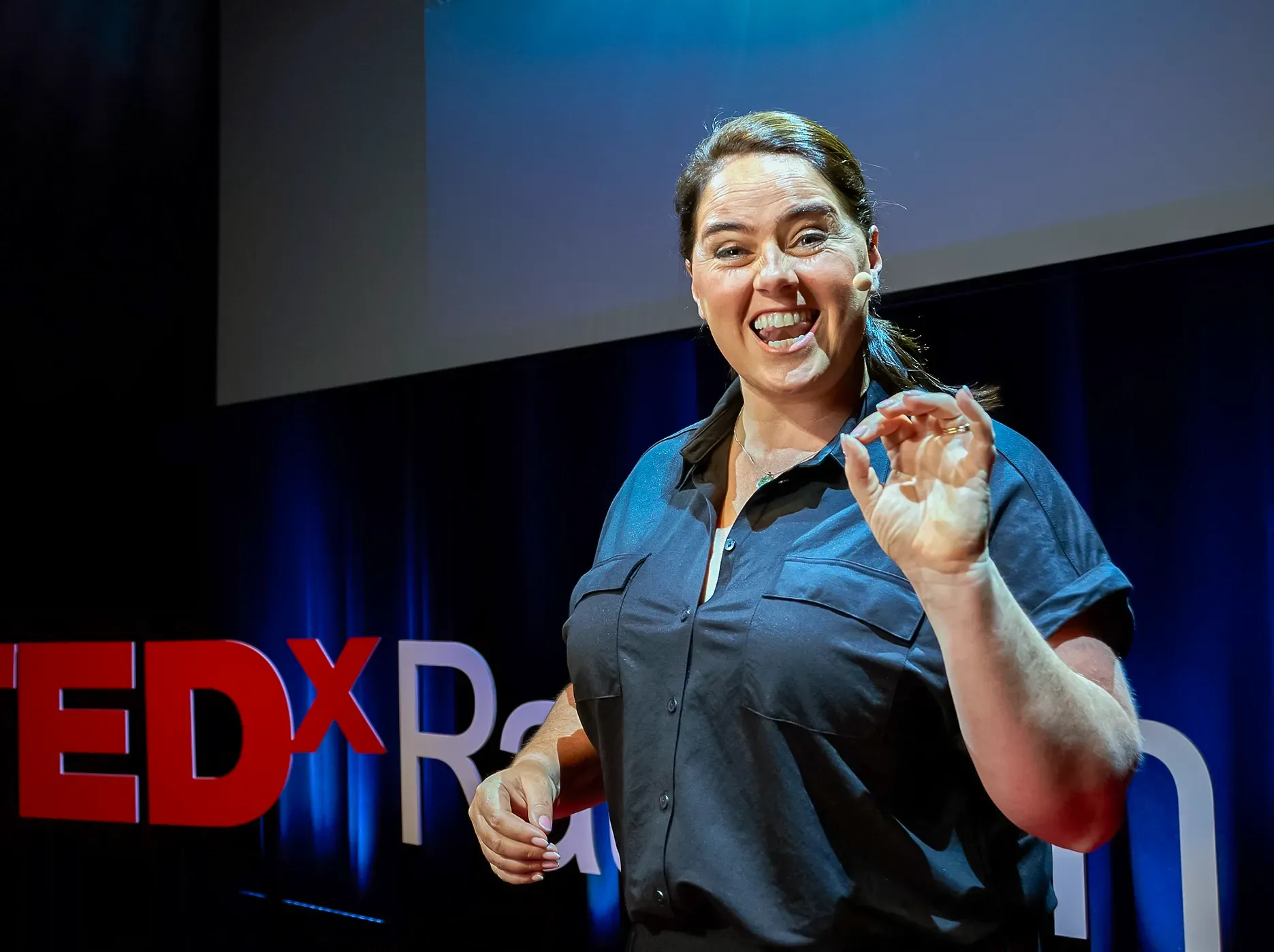 Woman on stage, gesturing, at a TEDx event with the logo