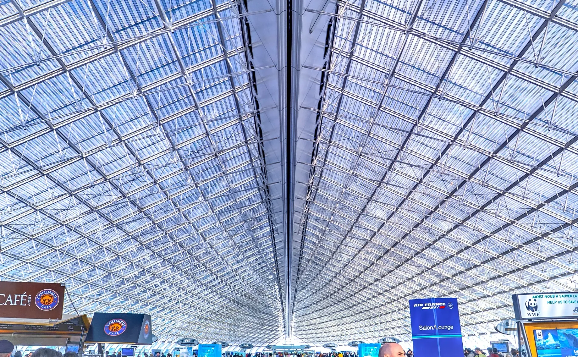 Spacious airport terminal with a vaulted glass-and-steel ceiling and overhead signage.