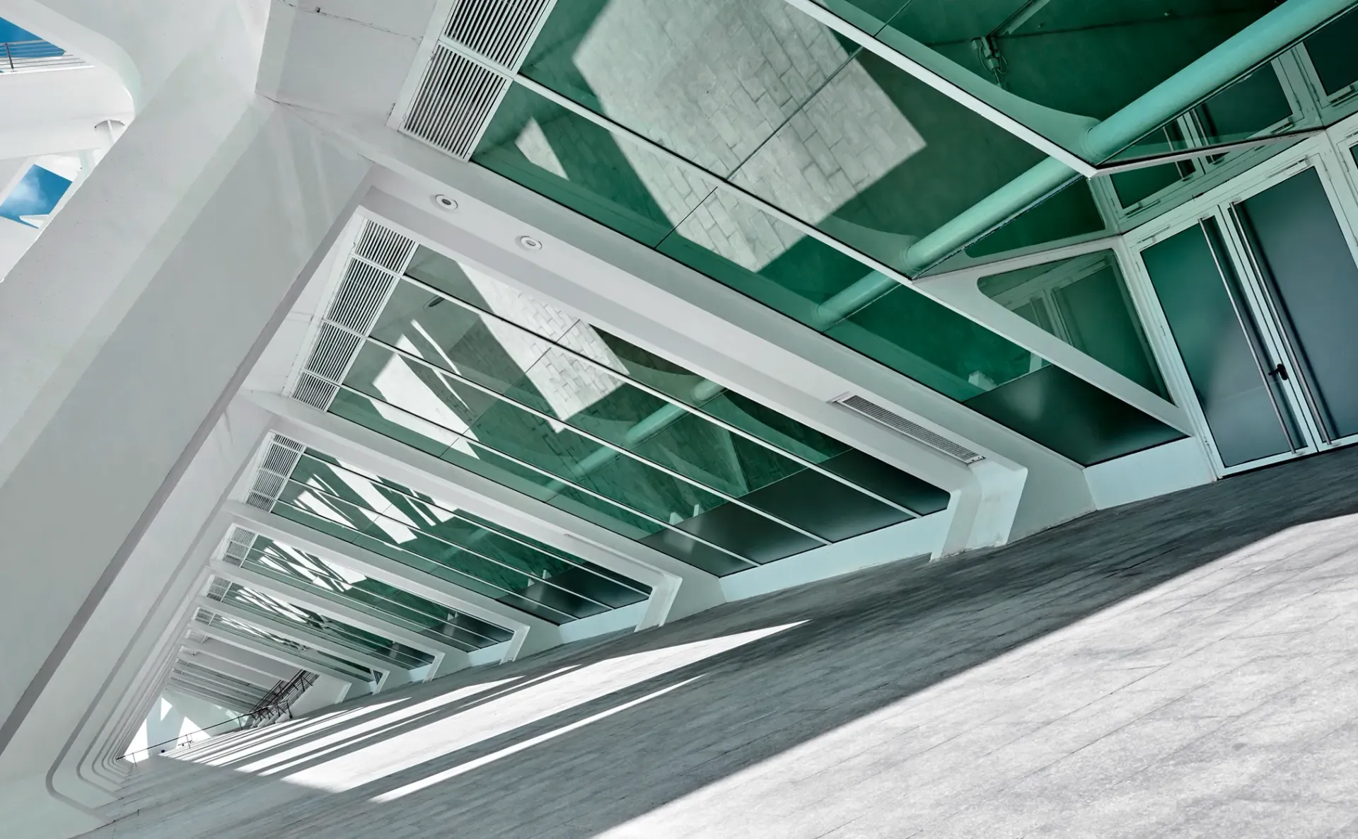Diagonal view of a modern white stairwell with green glass panels and metal railings