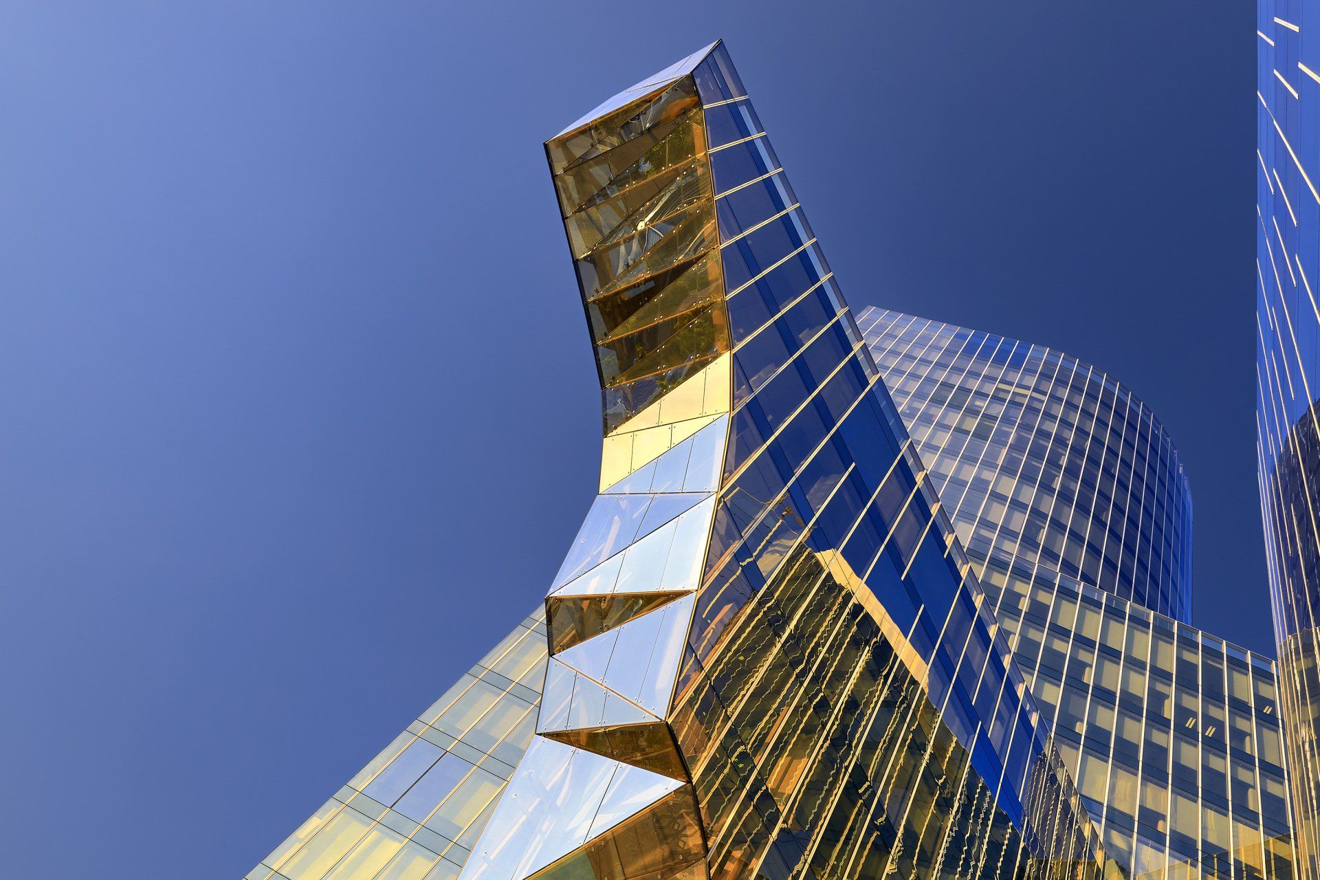 Modern glass skyscraper, angular design with blue and gold reflective surfaces against a clear blue sky.