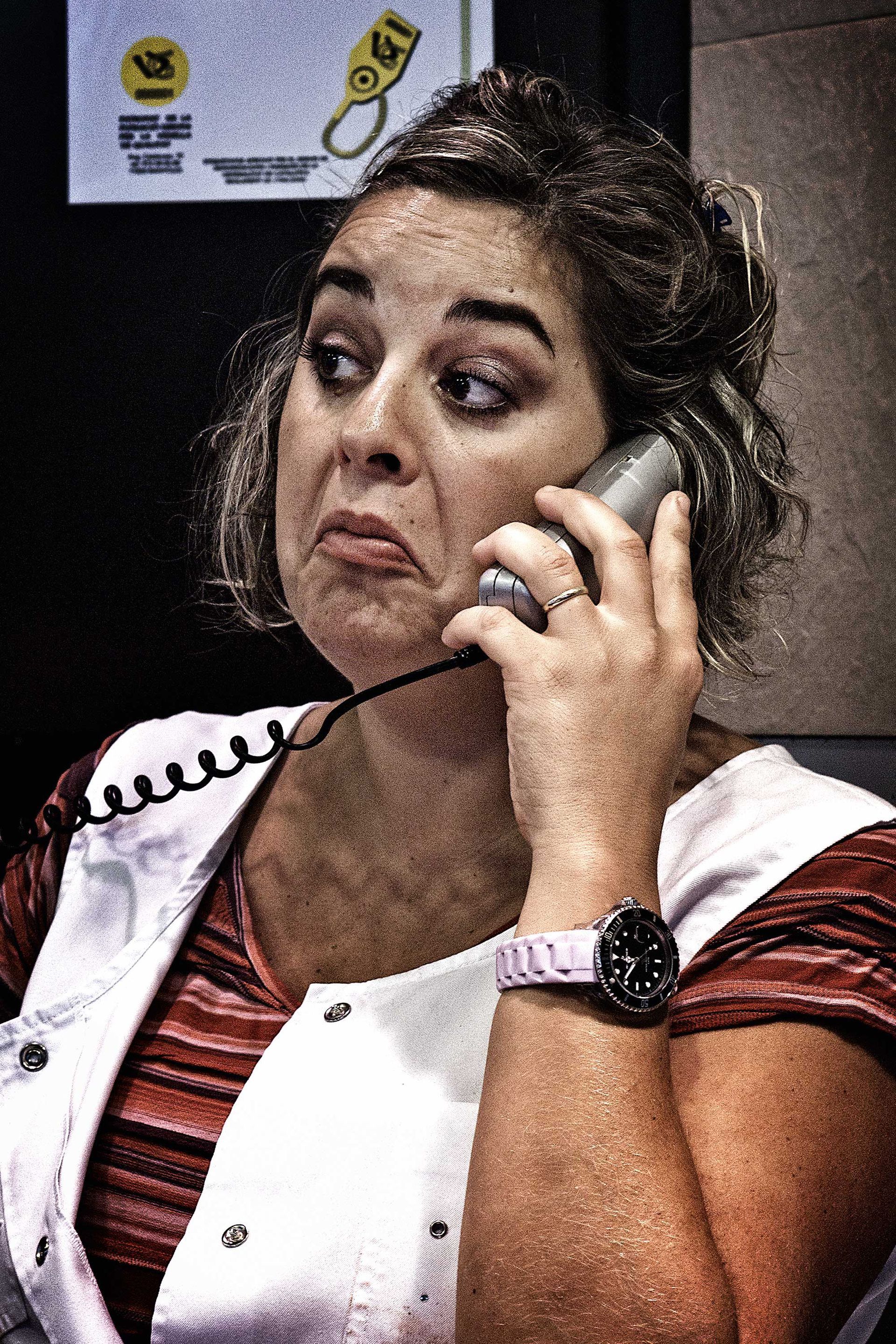 Woman on phone, making a frustrated face. Wearing a white vest over a striped shirt. Holding phone to her ear.