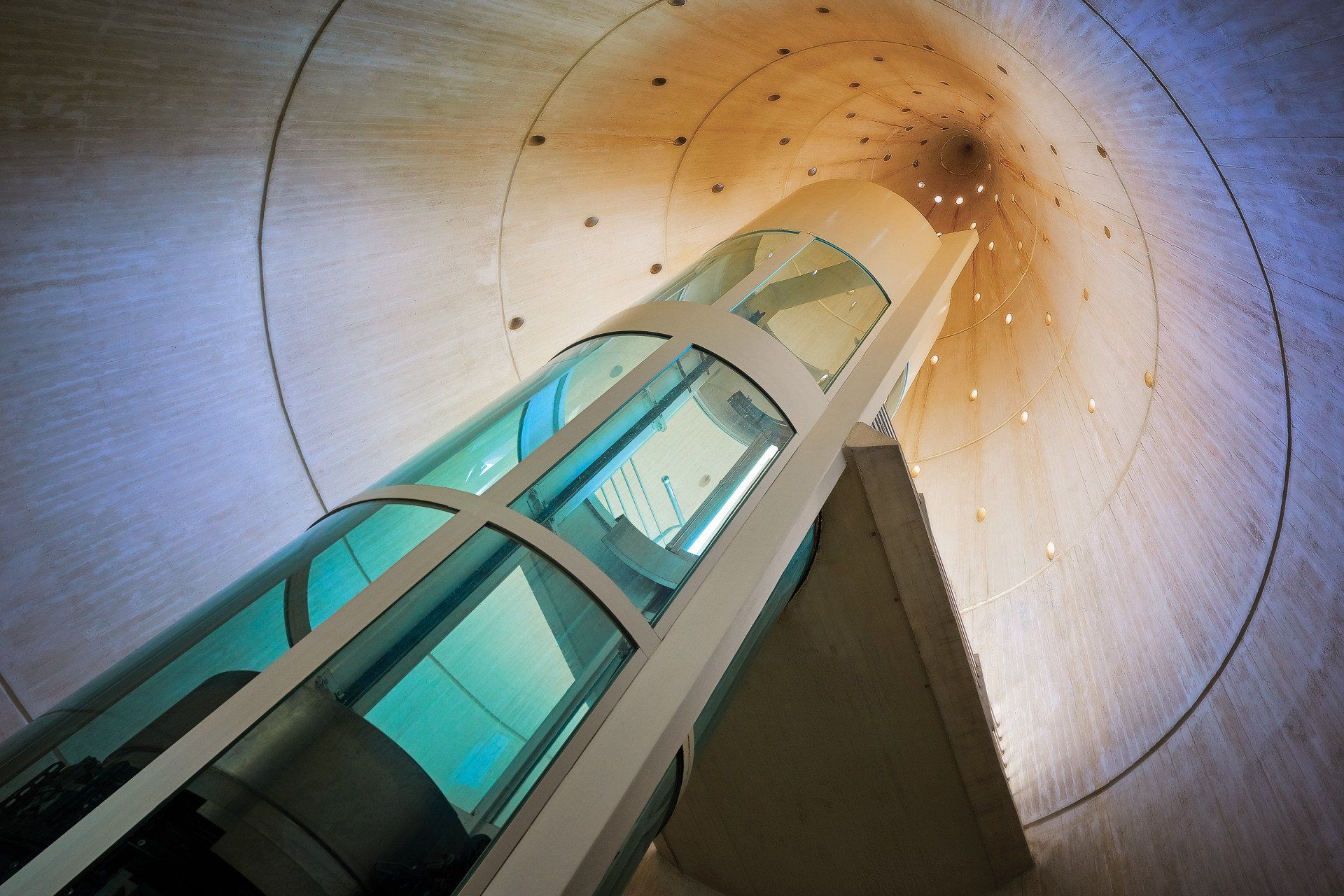 A glass elevator ascends through the center of a wide, conical wooden structure.