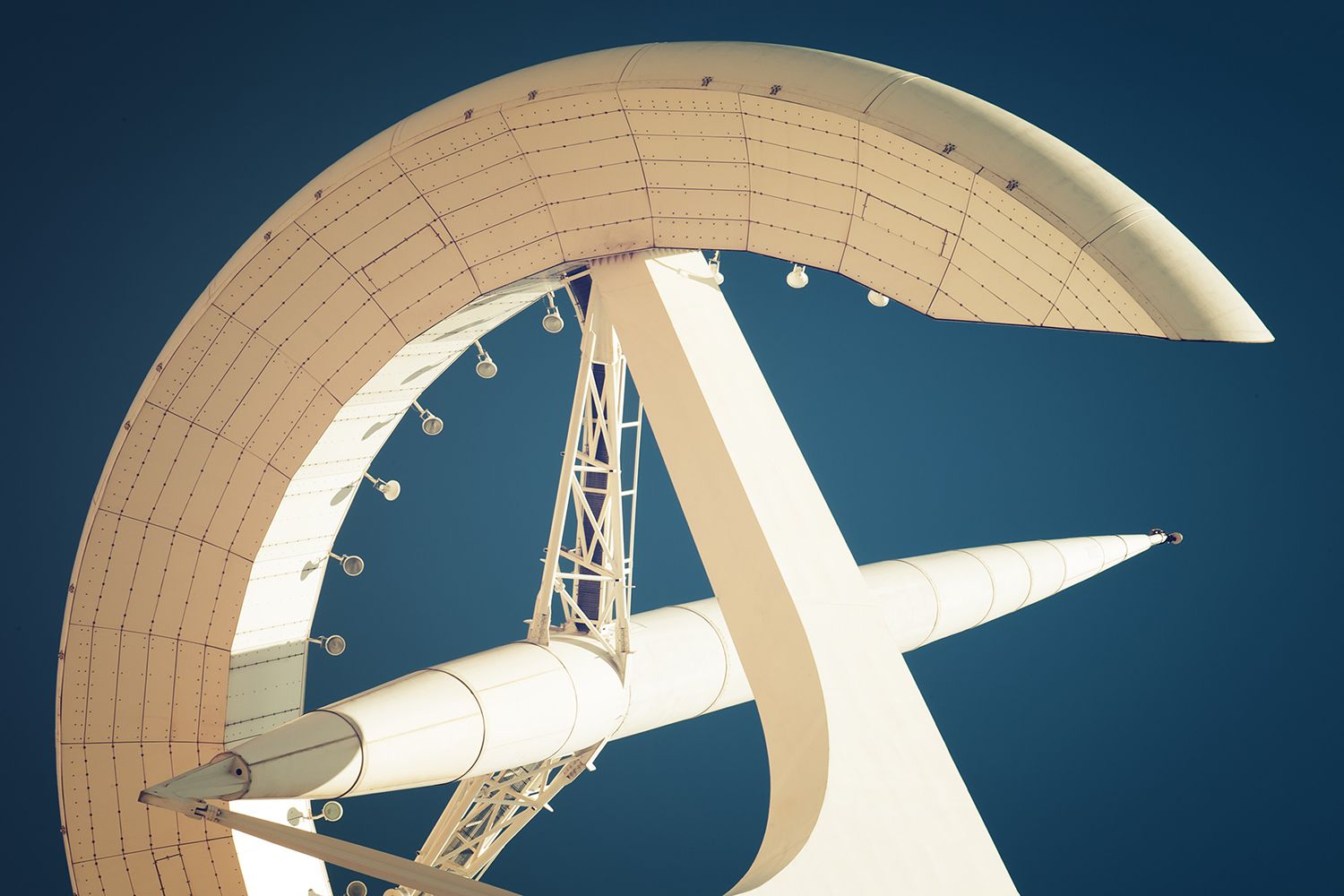 A stylized, cream-colored architectural structure resembling a crescent ring and a spire against a dark blue background.