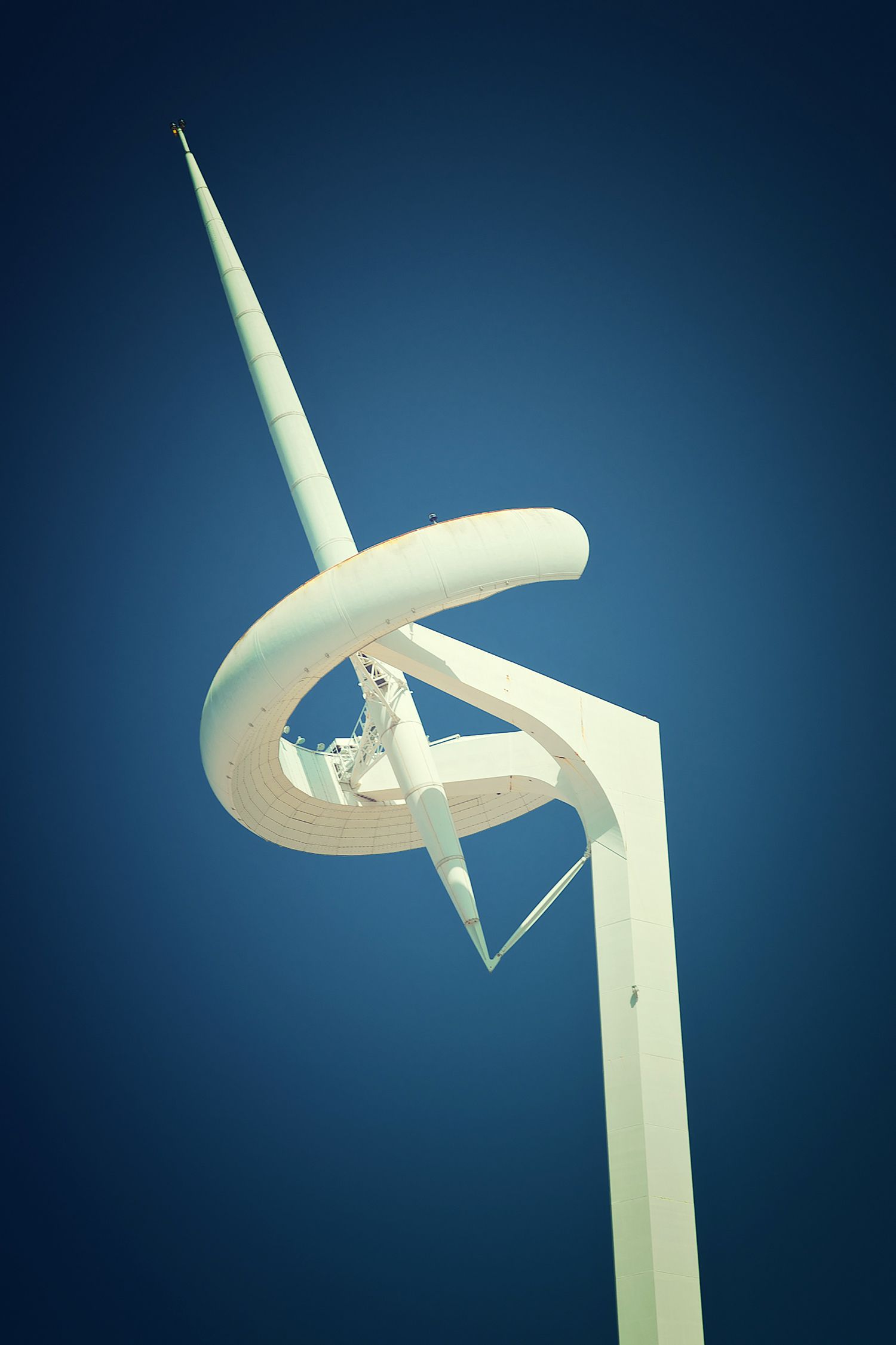 The Montjuïc Communications Tower in Barcelona, a white, curved steel sculpture-like tower against a deep blue sky.