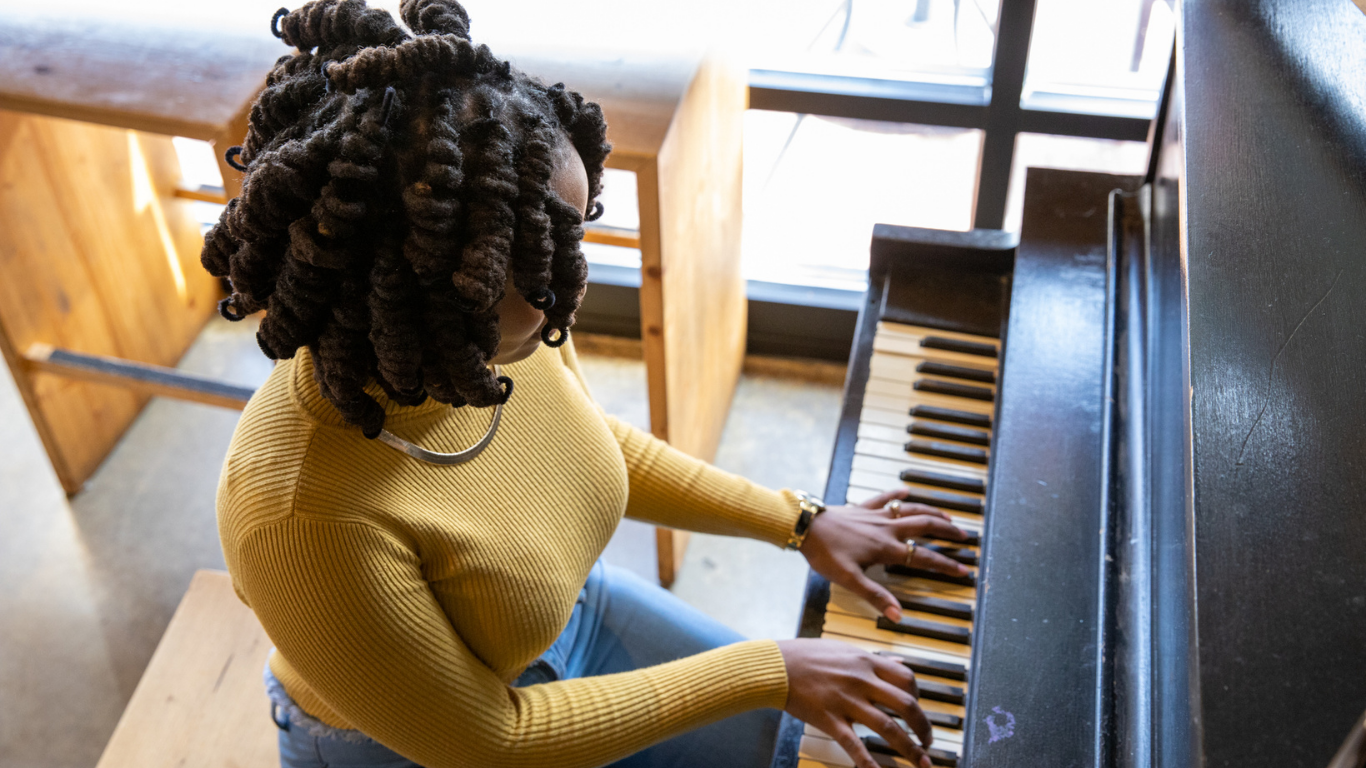 A woman in a yellow sweater is playing a piano.