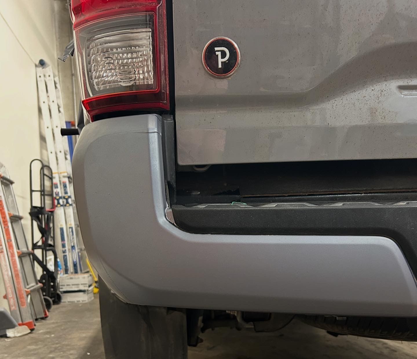 Close-up of a gray pickup truck’s rear corner and taillight in a garage or workshop