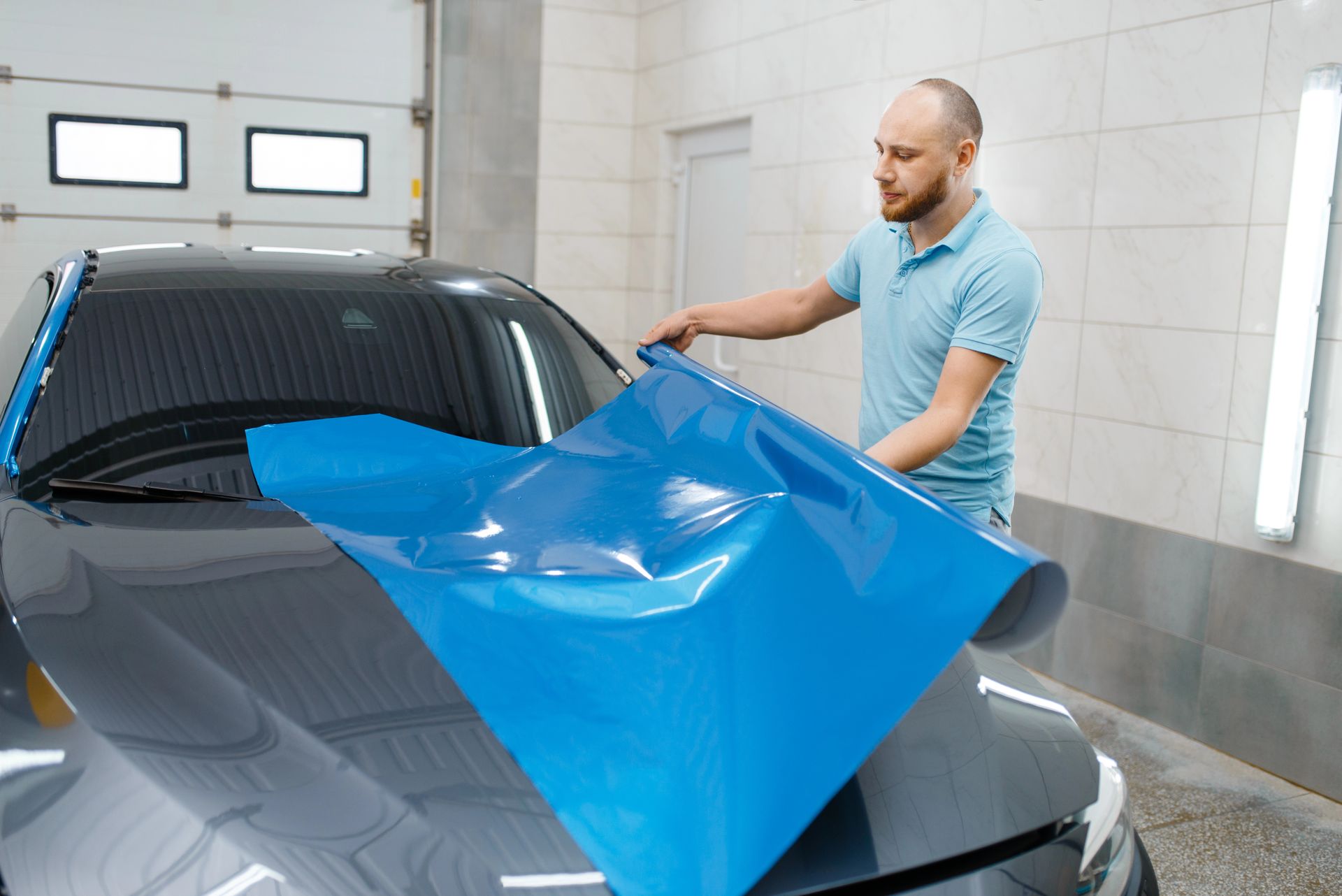 A man is wrapping a car with blue tape.